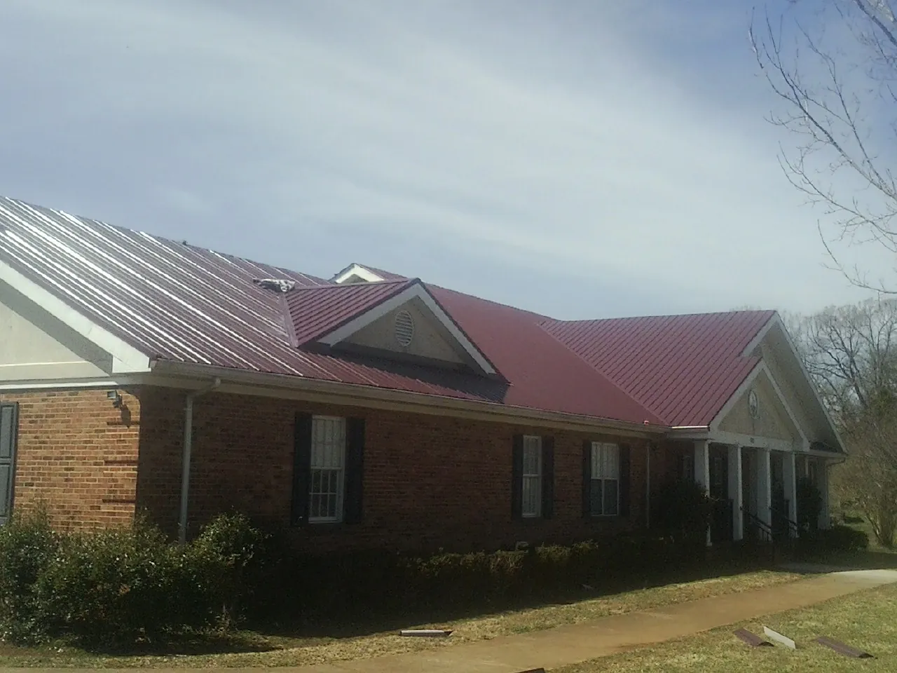 Red metal roof with gabled entries on a long brick building, from a Hail Damage Roof Repair job in Capon Bridge