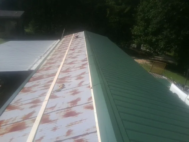 Old rusted panels beside newly installed green metal roofing — Wind Damage Roof Repair by Roofing Brothers in Capon Bridge