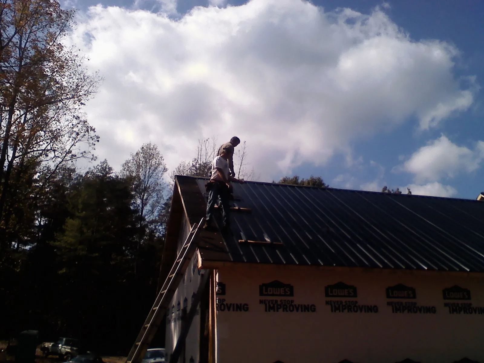 Roofer fastening dark metal panels high against a cloudy sky, from a Roof Inspection job in Capon Bridge