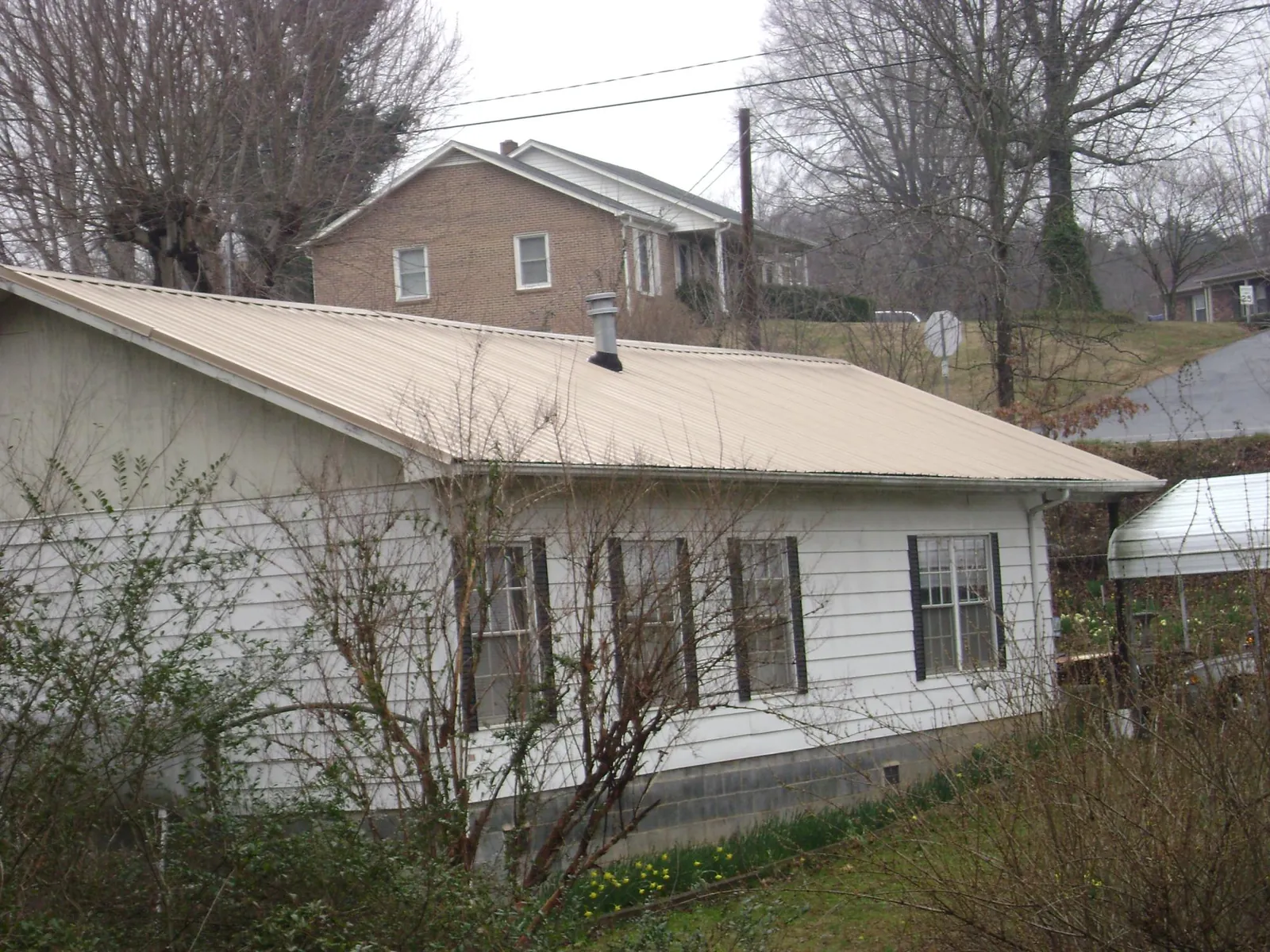 Tan metal roof on a white sided house set into a hillside — Commercial Roofing by Roofing Brothers in Capon Bridge